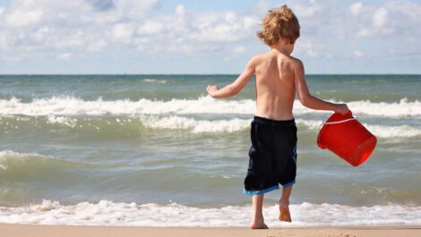 A boy holding a bucket runs into the water at a beach in MI