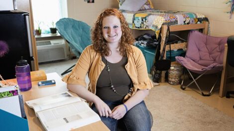 A happy college student sitting in her clean dorm room.