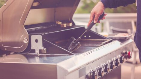 Person cleaning a gas grill with a brush.