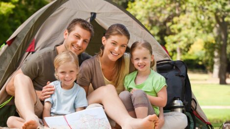 A young family smiling for a photo in front of their camping tent.