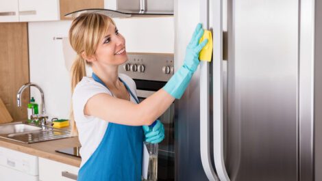 A young woman cleaning a refrigerator.