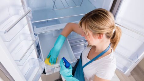 A young woman cleaning the inside of a refrigerator.