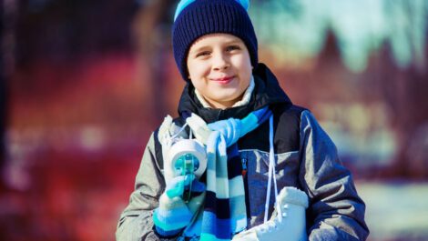 A young boy smiling for the camera with ice skates around his neck.