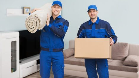 Two movers smiling carrying a rug and moving box.