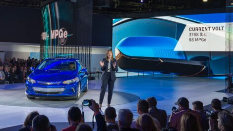 A vehicle showcased at the NAIS and a woman presenting to a crowd.