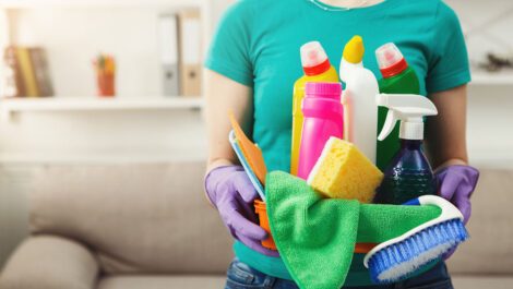 Young woman holding bucket with cleaning supplies.