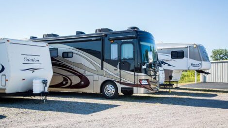 An RV and two trailers parked at a storage facility.