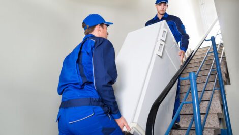 Two men moving a refrigerator up a flight of stairs.