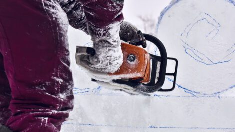A person carving with a chainsaw in the snow.