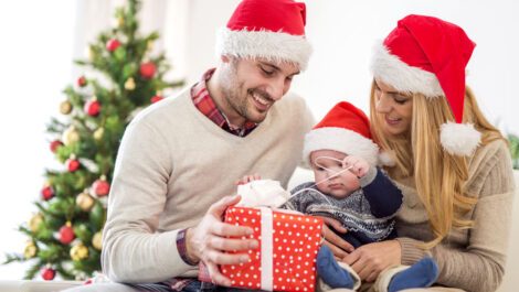 A mom and dad helping their baby open a Christmas present.