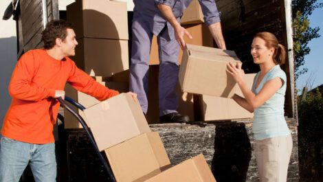 Three people carrying boxes out of a moving truck.