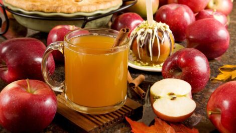 A glass of apple cider surrounded by apples and an apple pie.