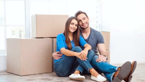 Young couple smiling next to moving boxes.