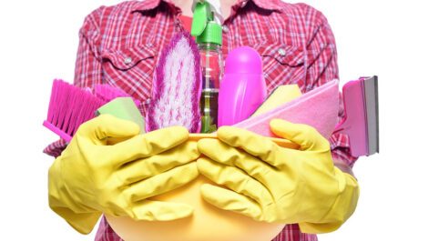 Lady wearing rubber gloves holding a bucket with cleaning supplies.