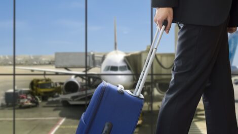 Man in suit rolling suitcase about to board a plane.