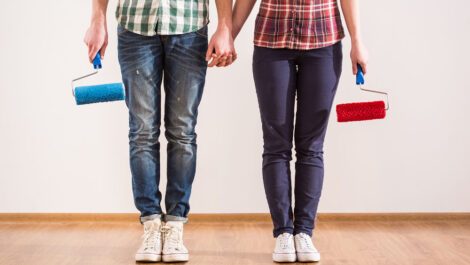 Man and woman holding hands carrying paint rollers.