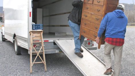 Two men loading a dresser into a moving truck.