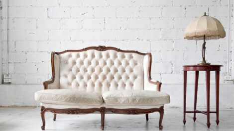 White antique couch next to a side table and lamp.