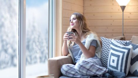 A young woman holding a mug looking out a window.