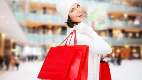 Woman smiling carrying three red shopping bags.