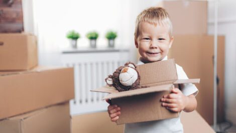 A smiling toddler that is packing toys surrounded by moving boxes.